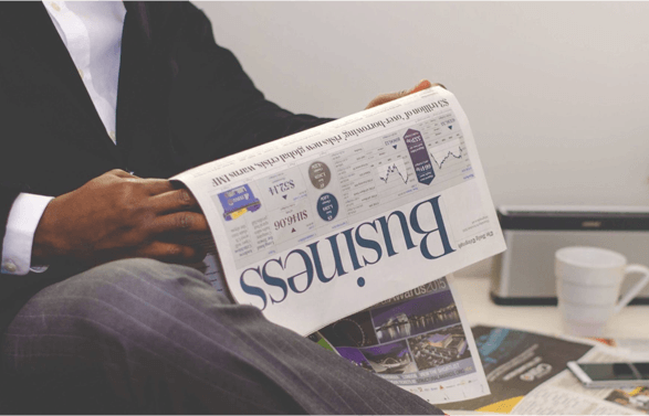 A man in a suit holding a newspaper with the headline Business